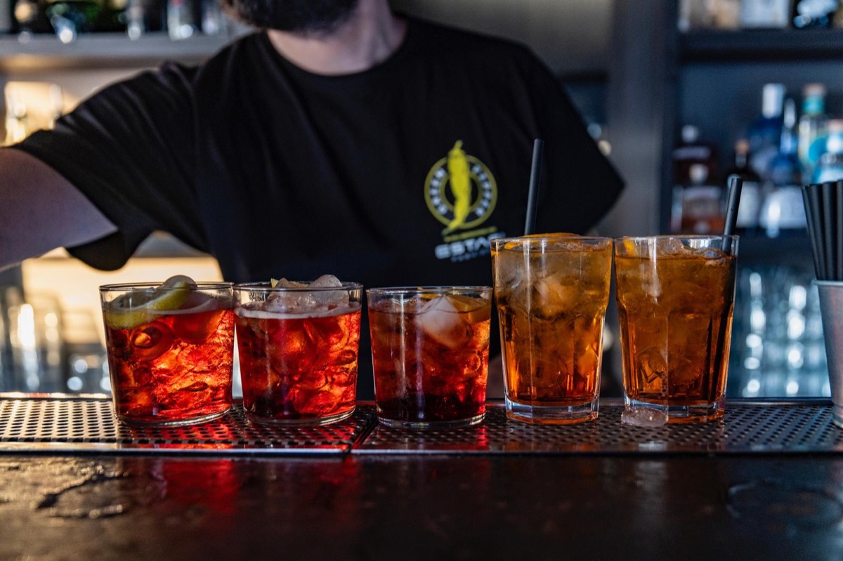 Cinque cocktail rossi e ambrati allineati sul bancone